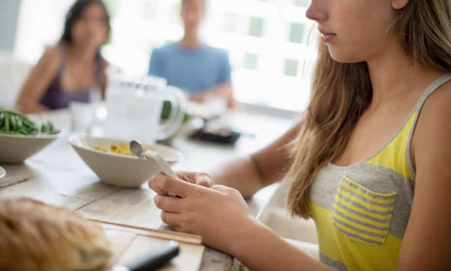Teenage girl at dining table using phone.