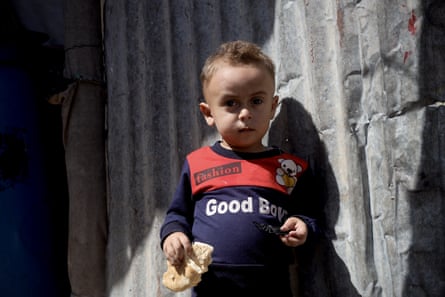 A small child holds a piece of bread next to a shelter