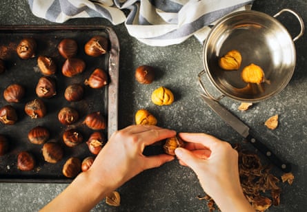 A pair of hand’s peeling a tray of roasted chestnuts