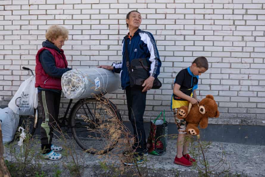 People attach blankets they received as humanitarian aid to their bicycle, as a child holds a teddy bear in Moshchun, Ukraine.