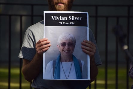 A man stands in front of black railings holding a picture of a woman, who name is written on a black band at the top