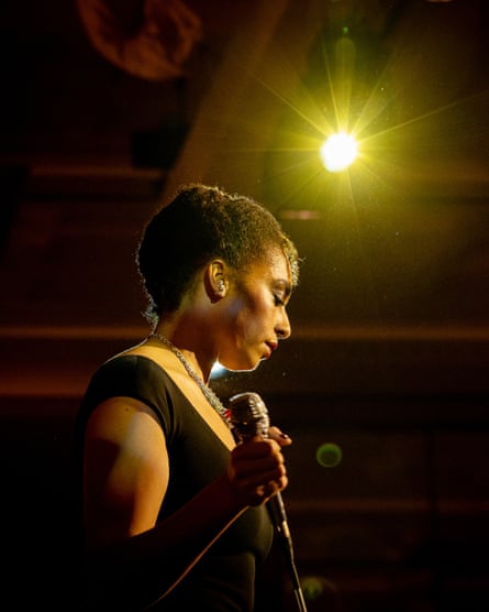 Celeste holding a microphone and wearing a black dress, with a bright spotlight shining above her