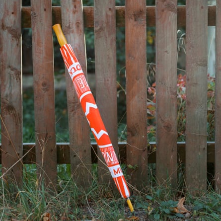A closed red and white patterned umbrella leans against a wooden fence outdoors