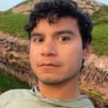 A person with short dark curly hair poses outside