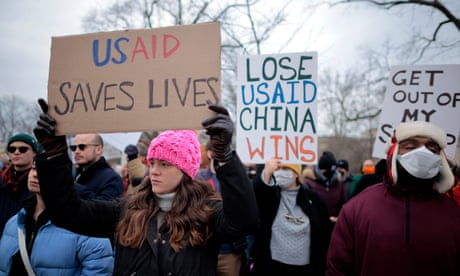 people hold signs that read 'USAID saves lives' and 'lose USAID China wins'