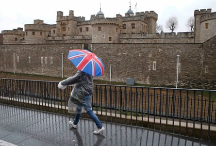 A tourist carrying a Union Flag umbrella passes the Tower of London.