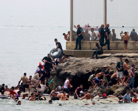 People clamber out of the sea on to a rocky outcrop