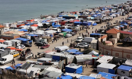 Tightly packed tents, makeshift buildings and vehicles next to the sea