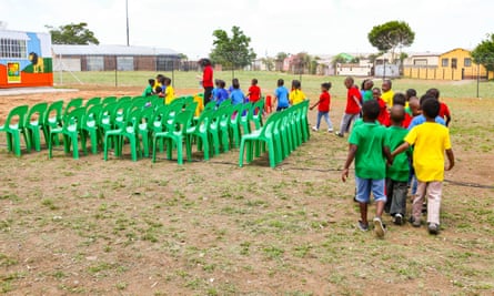 Schoolchildren wearing T-shirts in primary colours walk in twos towards an outdoor classroom