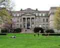 Students relax and play on a lawn in front of a neoclassical stone building with columns.