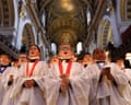 Choristers in white robes holding lit candles sing inside St Paul's Cathedral