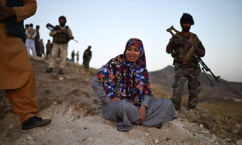 Salima Mazari sits on a hill observing the frontline against the Taliban surrounded by armed men.