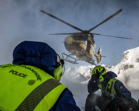 Two mountain rescue personnel crouch as an emergency helicopter lands in the French Alps