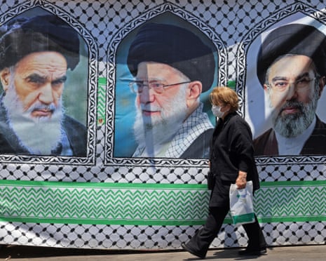 A woman wearing a face mask walks past a banner showing three portraits of religious leaders