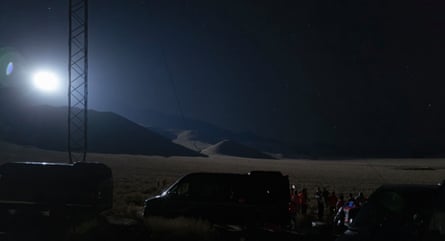 A bright spotlight beams over a desert at night as rescue teams test the technology nearby
