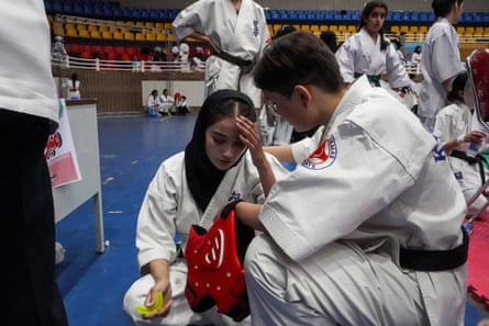 A young woman crouches with a hand to her head.
