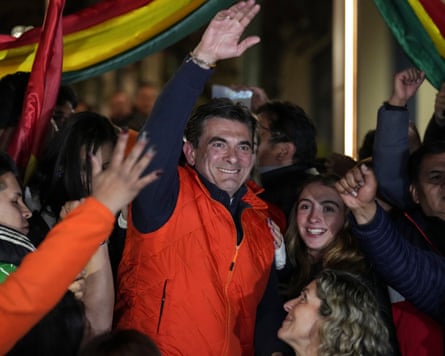 A man standing in a crowd raises his hand in a salutary greeting.