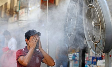 An Iraqi man wiping his face in front of two large misting fans