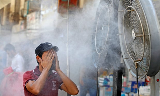 An Iraqi man wiping his face in front of two large misting fans