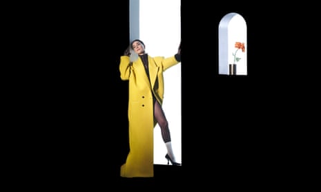 St Vincent in a white-lit stage set doorway in a yellow coat