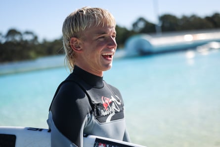 Hughie Vaughan is smiling and has his surfboard under his arm as he stands next to the pool at UrbnSurf in Sydney