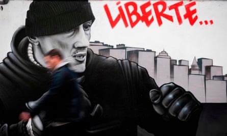 A man walks in front of a mural in Paris depicting Christophe Dettinger