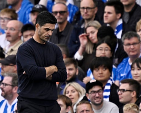 Arsenal manager Mikel Arteta stands with arms crossed, looking down with a troubled expression