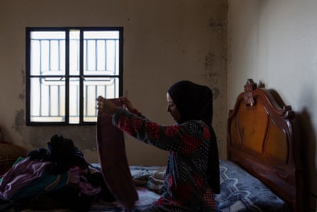 A woman in a headscarf in a dimly let room sits on a bed folding clothes
