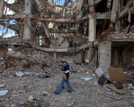 ईरान के तेहरान में इजरायली-अमेरिकी हमले में नष्ट हुई इमारतों के बीच से गुजरती एक महिला