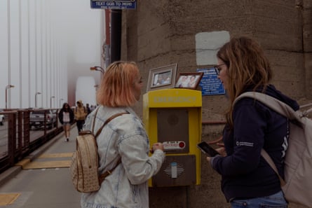 women look at call box with framed photos of people on top