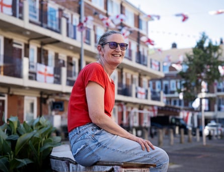 A woman in a T-shirt and jeans sits on a wall in front of a council estate with England flags on some balconies