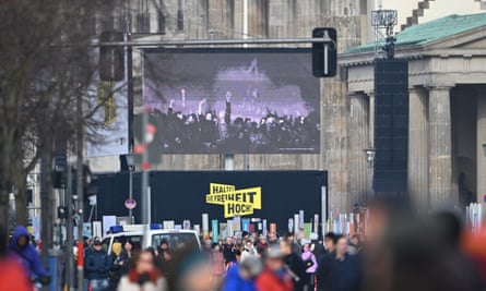 A screen displays footage from 1989 at the Brandenburg gate.