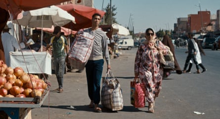 Aicha Tebbae and Abdellah El Hajjouji as mother and son walk down a market street carrying large bags in a still from The Damned Don’t Cry