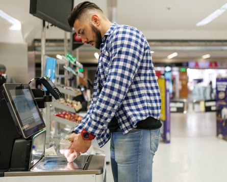A man in a checked shirt at the self-service checkout in a supermarket.