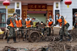 People in military fatigues wearing facemasks use shovels to move muddy debris into a small trailer
