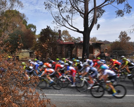 Cyclists ride past a burned out house during the 2020 Women’s Tour Down Under