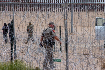 A uniformed official stands behind a wall of concertina wire