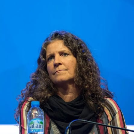 A woman with curly hair sits at a microphone.