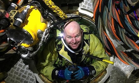 Chris Lemons in the diving bell, wearing an underwater suit with a yellow helmet beside him, and wires and equipment visible.