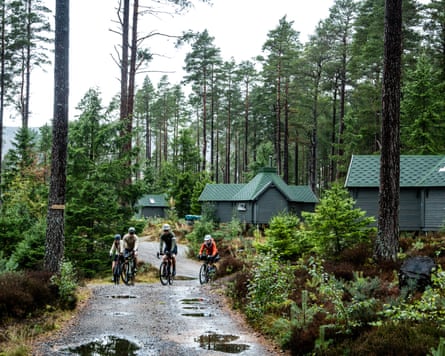 A group of people cycling through a woody area with green cabins