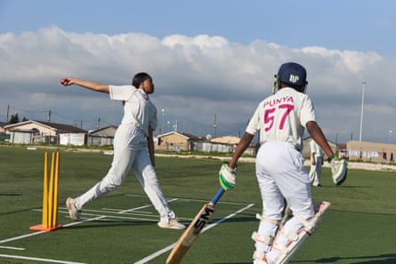 A tall African girl bowls from next to a set of stumps as a boy with a bat prepares to run