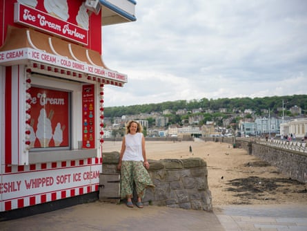 A woman stands against a wall next to an ice-cream shop in front of a beach