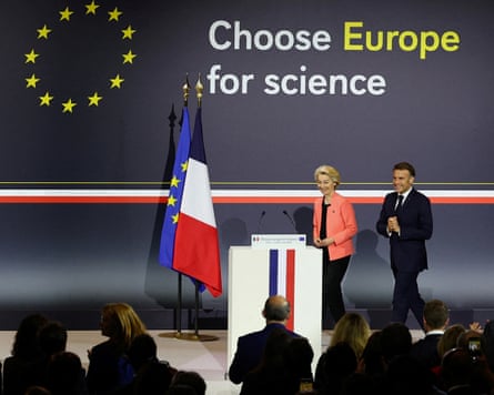 Two people walk on to a stage with a French and European flag behind a lectern