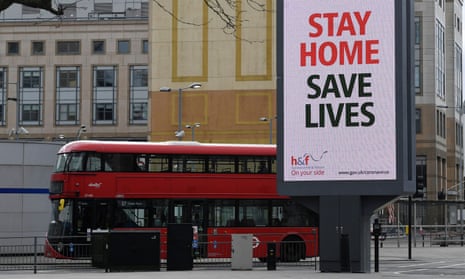 A red London bus drives past a government sign advising people to stay home.