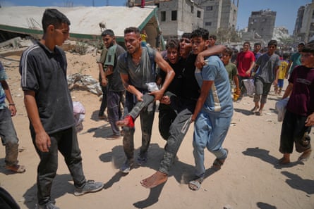Palestinians carry a man who was wounded while rushing to collect humanitarian aid airdropped by parachute into Gaza City on Thursday.