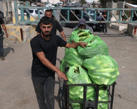 Palestinians pass a military gate, one pushing a cart piled with bagged produce.