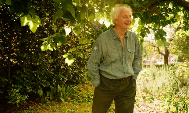Philip Pullman standing with his hands in his pockets in his garden, smiling