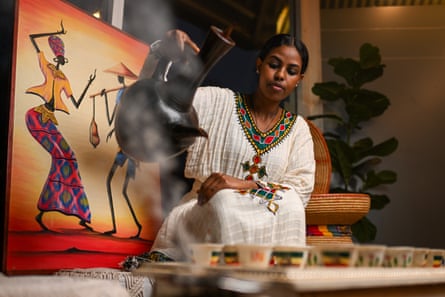 A woman in a white dress pours coffee from a black pot for a traditional Ethiopian coffee ceremony.