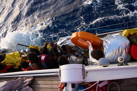 People by rail on deck of Nadir; some have gold and silver foil blankets and others wear life vests.
