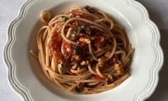 A bowl with scalloped edges containing a pile of spaghetti swirled around with sauce on top
